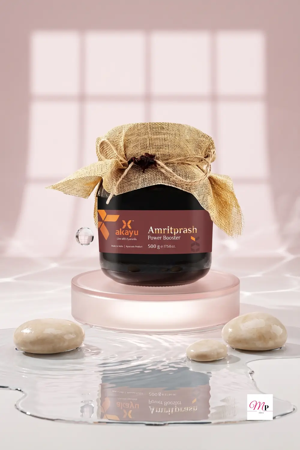 Akayu Amritprash Power Booster ayurvedic chyawanprash in a dark glass jar with burlap cover on a reflective water surface with soft window light