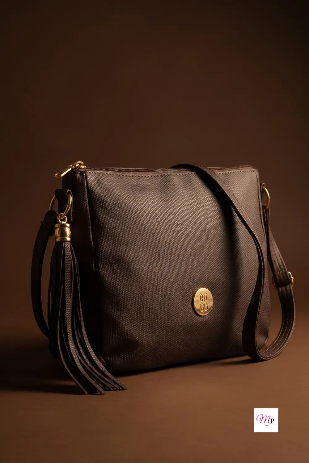 Close-up studio shot of Baggit Kurama sling bag showing textured vegan leather grain, gold logo medallion, and tassel charm