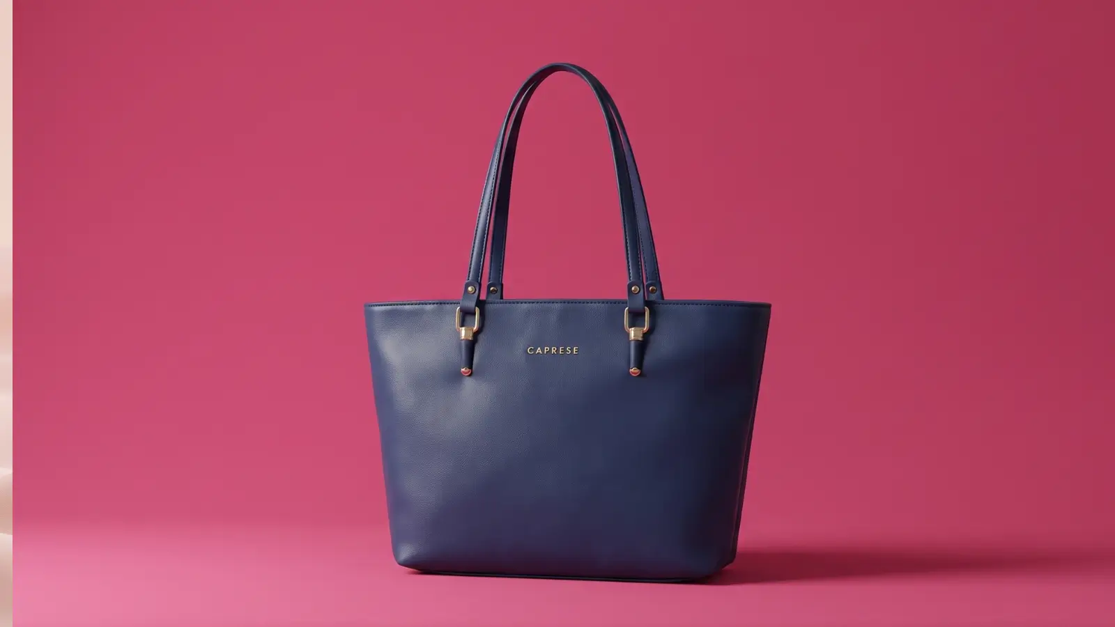 Caprese navy blue faux leather laptop tote bag with gold hardware against pink studio background
