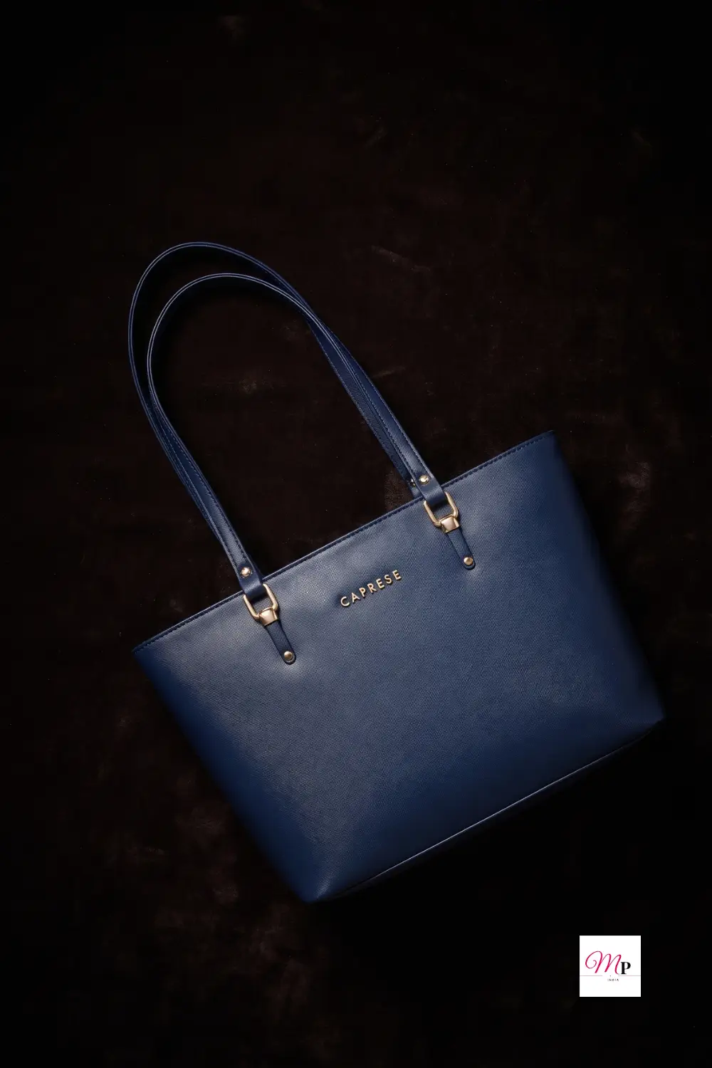 Navy blue Caprese faux leather tote bag on dark surface with dramatic studio lighting