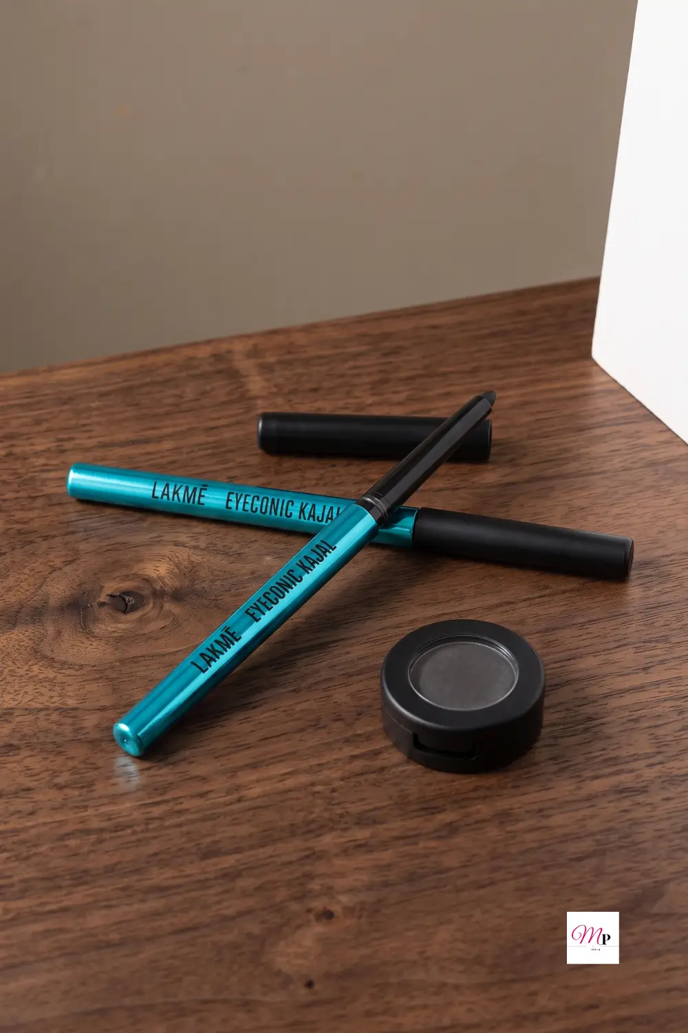 Two Lakme Eyeconic Kajal pencils crossed on wooden surface with black pigment pot