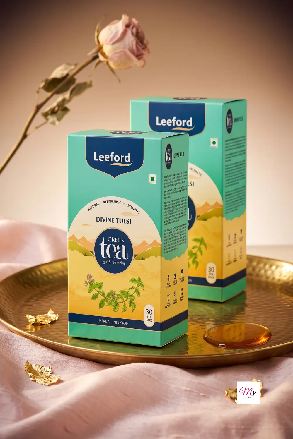 Leeford Divine Tulsi Green Tea for immunity and metabolism in teal boxes on a gold tray with dried rose and honey drizzle