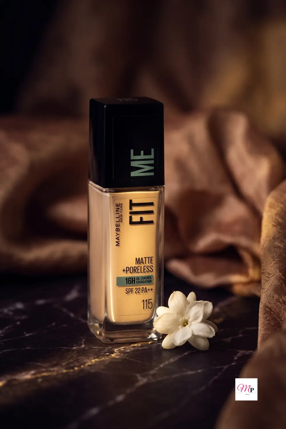 Maybelline Fit Me Foundation bottle with white jasmine flower and silk fabric on dark marble surface
