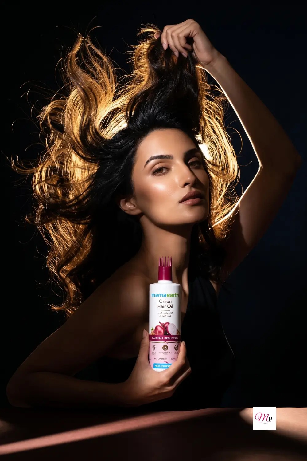 Woman with voluminous hair holding Mamaearth Onion Hair Oil for hair fall control