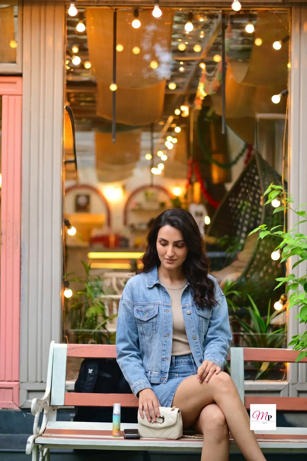 Light wash denim jacket outfit detail shot seated at outdoor cafe with warm ambient lighting