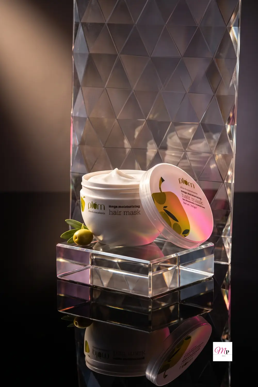 Plum Olive Macadamia hair mask on acrylic pedestal with crystal backdrop and warm light reflections — best hair mask for frizzy hair India