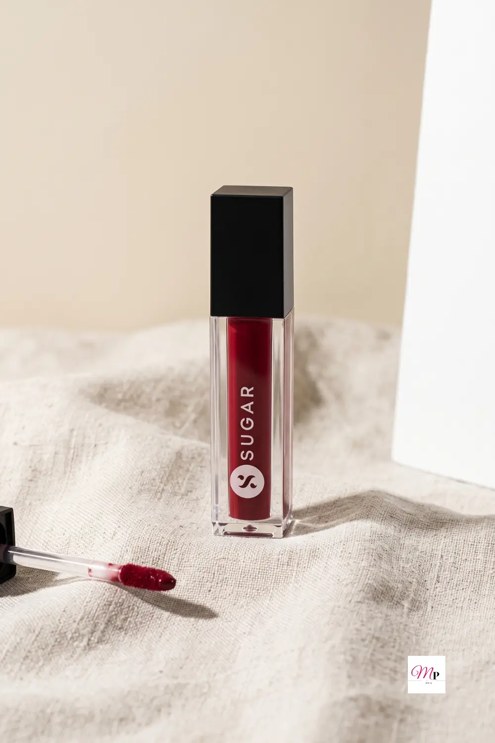 SUGAR Smudge Me Not Mini Drop Dead Red lipstick tube with applicator wand on soft linen fabric showing doe-foot applicator detail | SUGAR Smudge Me Not Mini Drop Dead Red lipstick applicator close-up