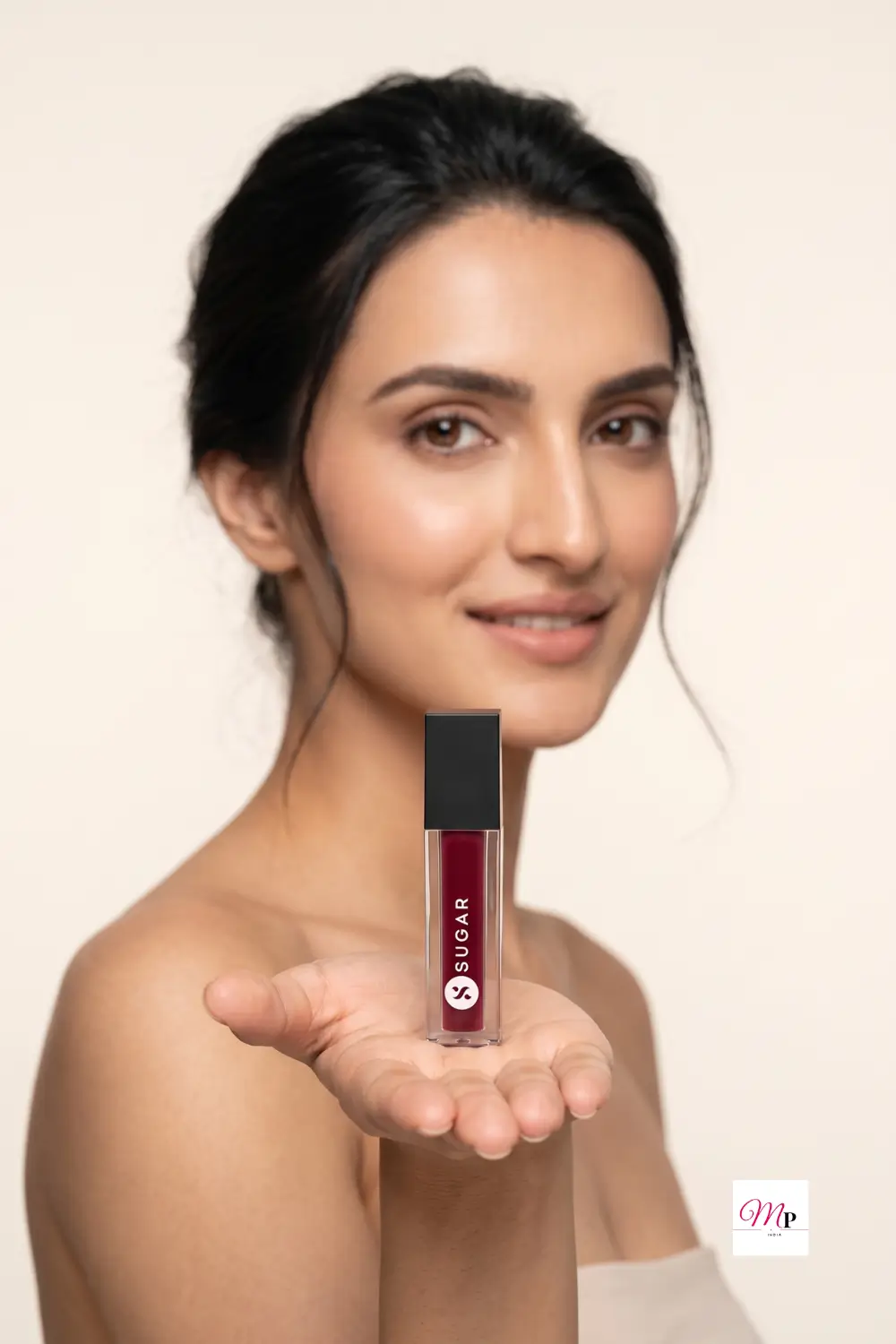 Model smiling and holding SUGAR Smudge Me Not Mini Drop Dead Red lipstick in open palm against soft cream background | SUGAR Smudge Me Not Mini Drop Dead Red lipstick gift presentation