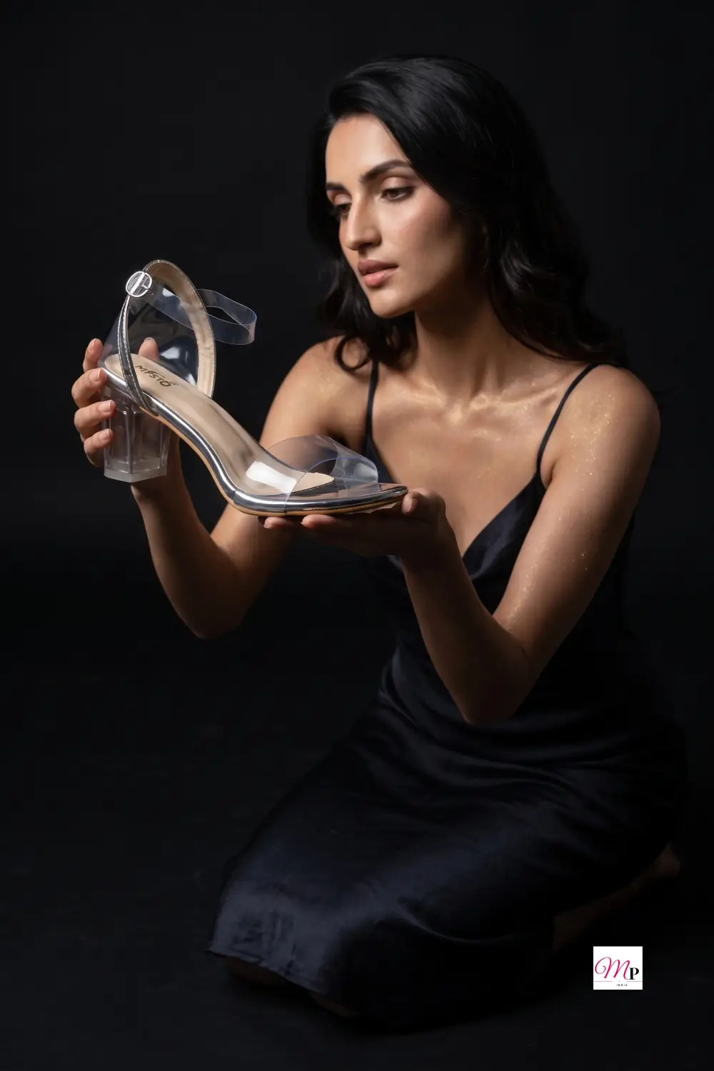 Misto transparent silver heels held in hand showing clear ankle strap buckle and chrome trim