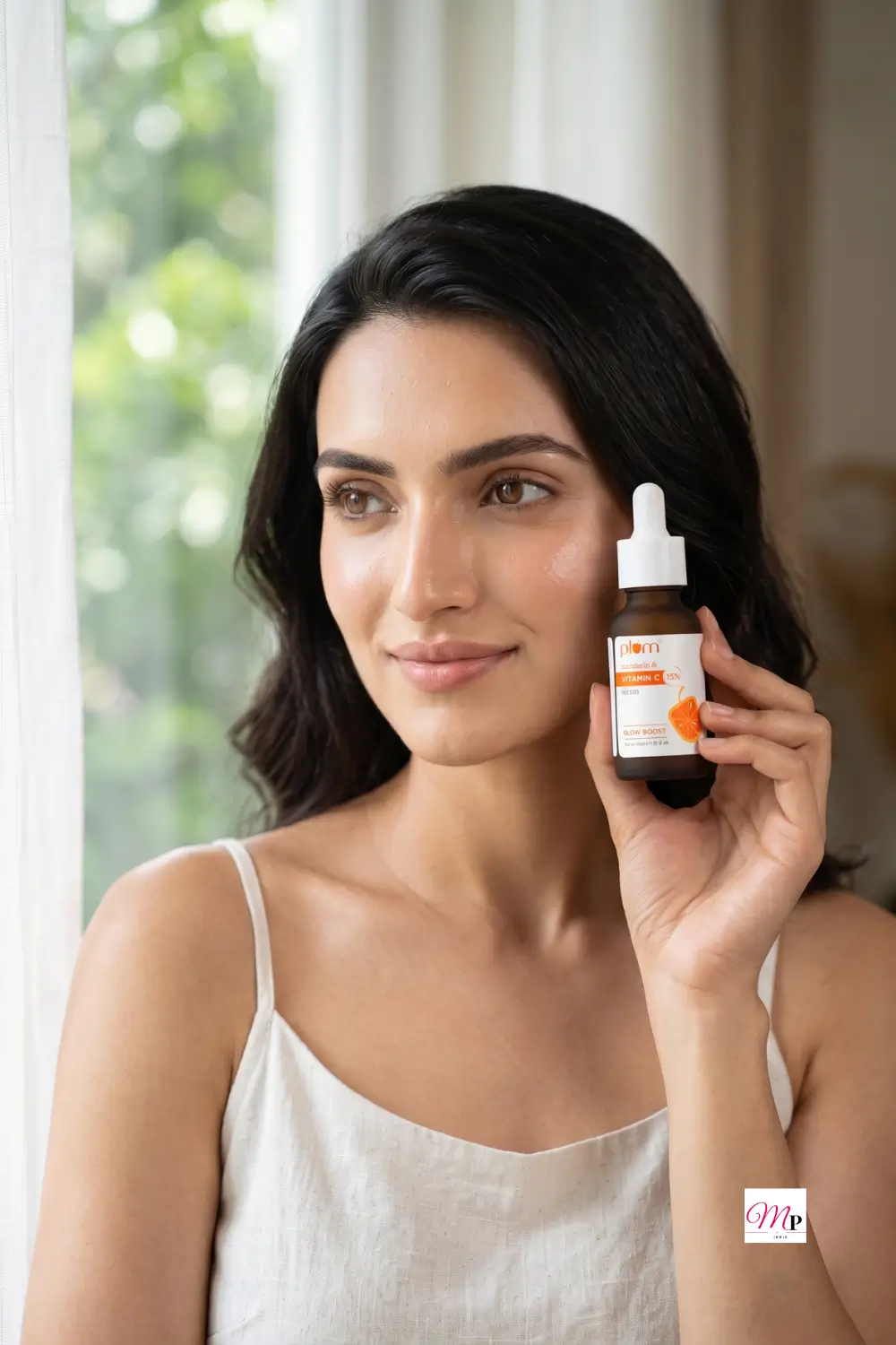 Woman holding Plum 15% Vitamin C serum for dark spots beside her face in soft morning window light with greenery