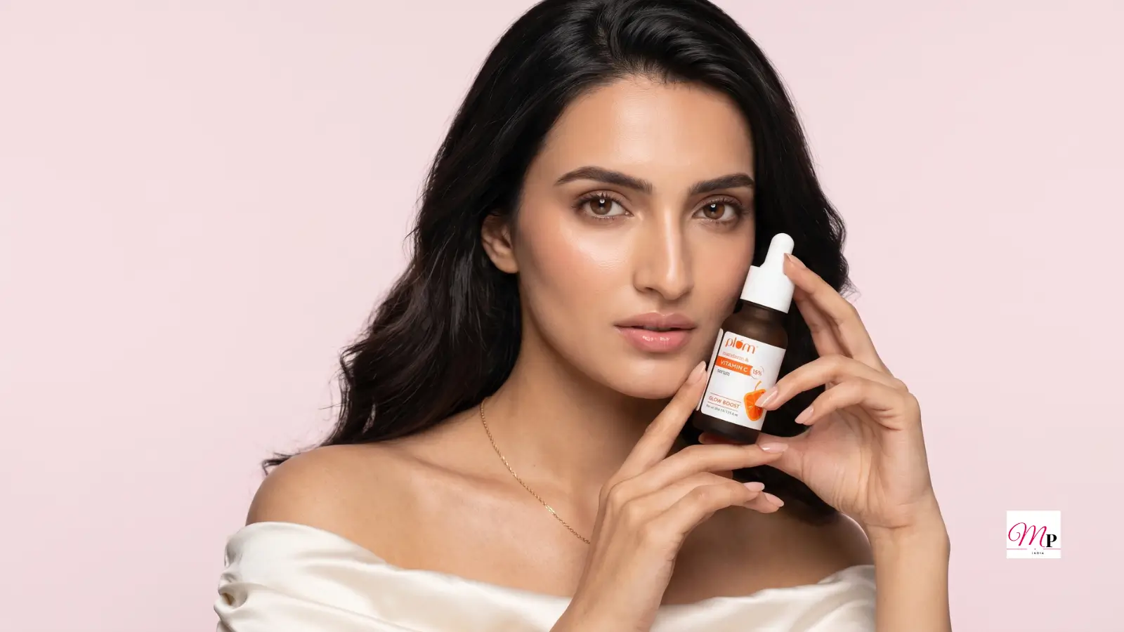 Plum 15% Vitamin C glow face serum for dark spots held by model against blush pink studio backdrop
